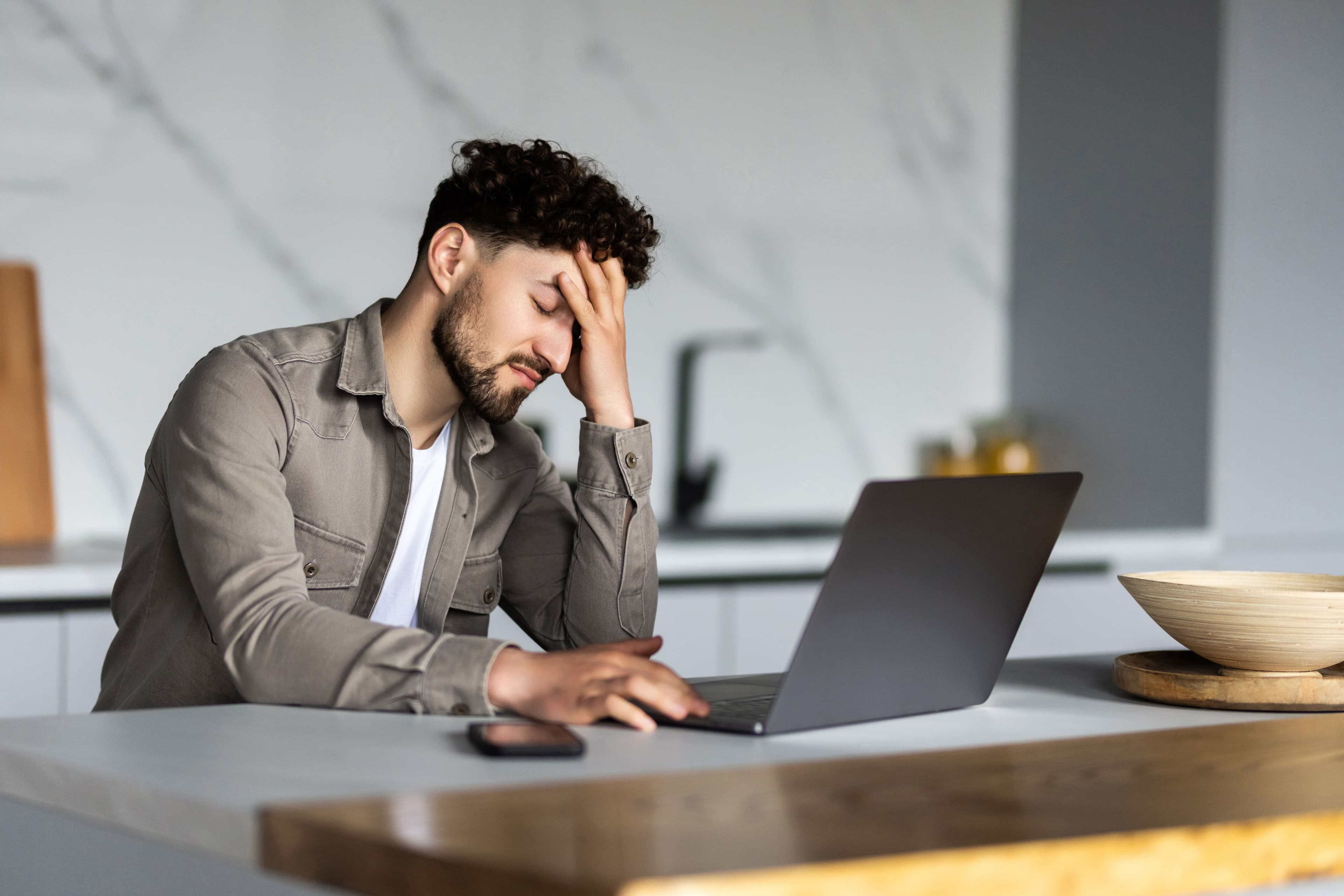 An employee working on a laptop with their hands on forehead