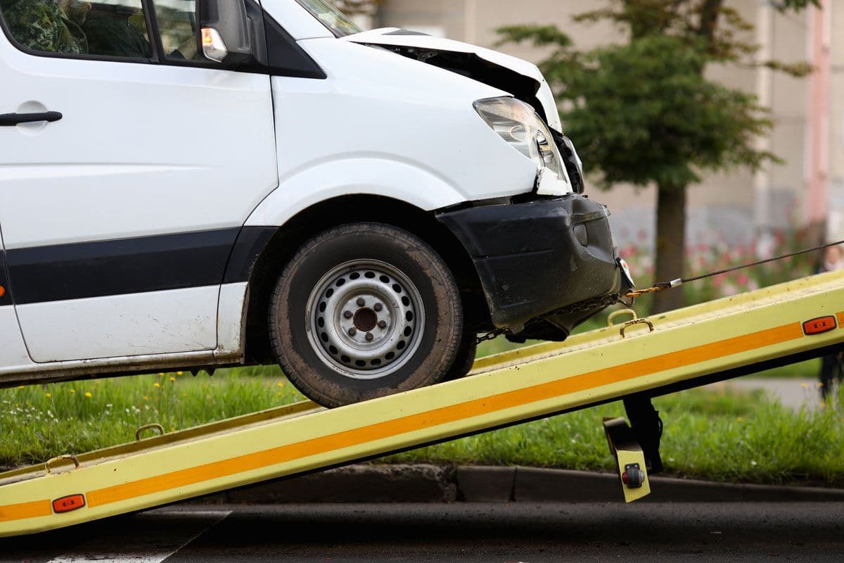 White van with crash damage to the bonnet being loaded on a flatbed truck